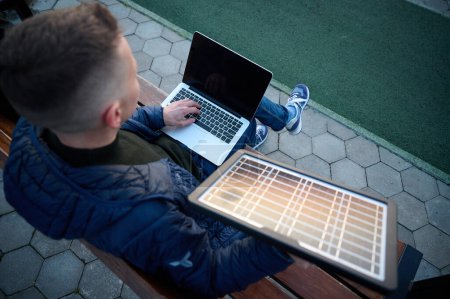 Photo for Confident businessman sitting on the bench and charging his laptop with portable solar panel. Concept of renewable energy. Green independent energy. Top view - Royalty Free Image
