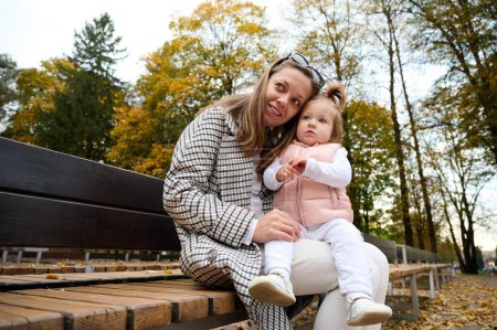 Photo for Mother and cute baby girl walking in autumn park with leaves on the ground. Mom spending time with a small child in the park. ?oncept of a good mother-child relationship. - Royalty Free Image