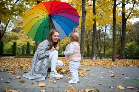 Photo for Mother and cute baby girl walking in autumn park with leaves on the ground. Mom spending time with a small child in the park. ?oncept of a good mother-child relationship. - Royalty Free Image