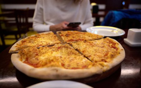 Téléchargez les photos : Vue rapprochée de la pizza sur la table. Délicieux repas. Les gens se réunissent dans la pizzeria ensemble ont plaisir à partager la nourriture italienne savoureuse - en image libre de droit