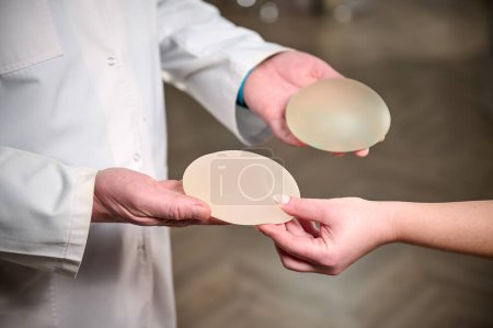 Photo for Close-up of female plastic surgeon demonstrates breast implants to a patient for her new breast. The plastic surgeon holds breast silicone implants. Breast augmentation concept. Breast Implant Samples - Royalty Free Image