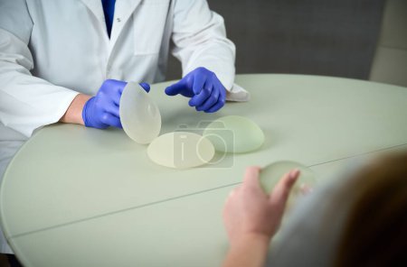 Close-up of female plastic surgeon demonstrates breast implants to a patient for her new breast. The plastic surgeon holds breast silicone implants. Breast augmentation concept. Breast Implant Samples