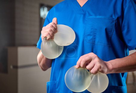 Téléchargez les photos : Un gros plan d'une chirurgienne plasticienne montre des implants mammaires à une patiente pour son nouveau sein. Le chirurgien plastique tient des implants en silicone mammaire. Concept d'augmentation mammaire. Échantillons d'implants mammaires - en image libre de droit