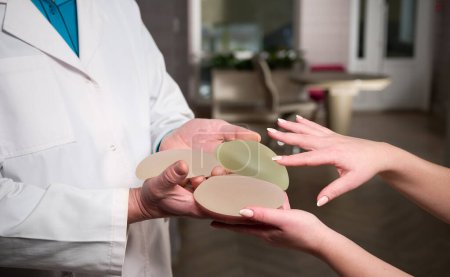 Photo for Close-up of female plastic surgeon demonstrates breast implants to a patient for her new breast. The plastic surgeon holds breast silicone implants. Breast augmentation concept. Breast Implant Samples - Royalty Free Image