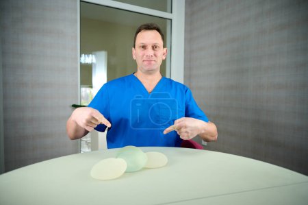 Foto de La cirujana plástica muestra implantes mamarios a una paciente para su nueva mama. El cirujano plástico sostiene los implantes de silicona mamaria. Concepto de aumento de senos. Muestras de implantes mamarios - Imagen libre de derechos