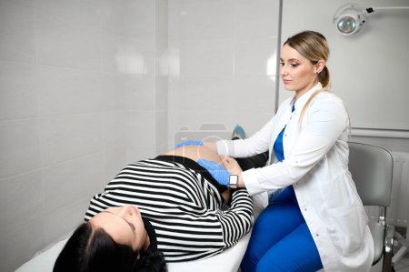 Foto de Guapa ginecóloga doctora consultando a mujer embarazada. Examinar y consultar a una paciente joven embarazada en la clínica.Examen obstétrico. Control de salud del bebé y la madre. Salud de la mujer - Imagen libre de derechos