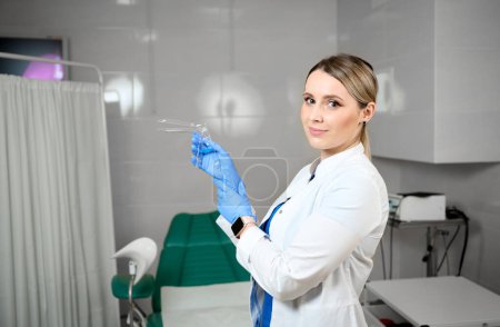 Photo for Pretty female doctor gynecologist in blue medical sterile gloves holding vaginal speculum. Women's health. Prevention illness. Early detection of cancer. Examining and consulting patient in clinic. - Royalty Free Image