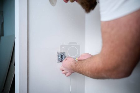 Photo for Crop view of electrician installing electric socket using screwdriver at construction site. Power socket installation. Installing a power outlet in to a plastic box on a wall. - Royalty Free Image