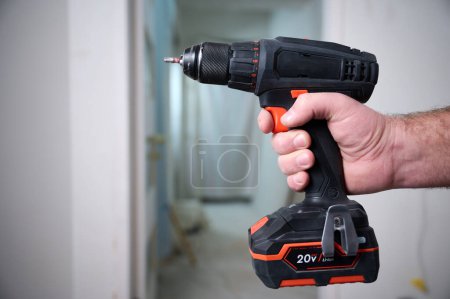 Photo for Construction worker holding electric cordless screwdriver in hand at construction site. Accessories for assembling, install furniture, repair home. Home renovation, electric tool for job. Crop view. - Royalty Free Image