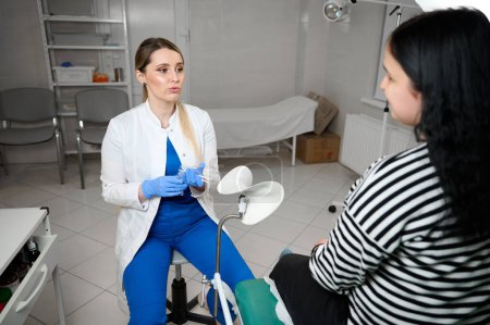 Pretty female doctor gynecologist in blue medical sterile gloves holding vaginal speculum. Obstetrical examination. Baby and mother healthcare check up. Women's health.