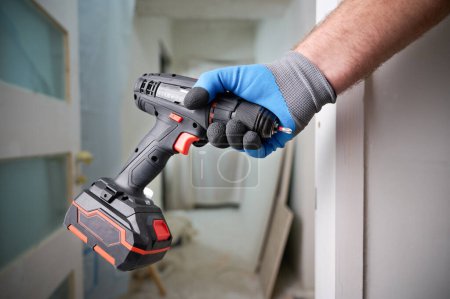 Photo for Construction worker holding electric cordless screwdriver in hand at construction site. Accessories for assembling, install furniture, repair home. Home renovation, electric tool for job. Crop view. - Royalty Free Image