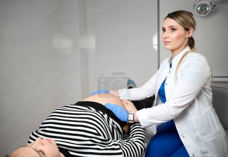 Foto de Guapa ginecóloga doctora consultando a mujer embarazada. Examinar y consultar a una paciente joven embarazada en la clínica.Examen obstétrico. Control de salud del bebé y la madre. Salud de la mujer - Imagen libre de derechos