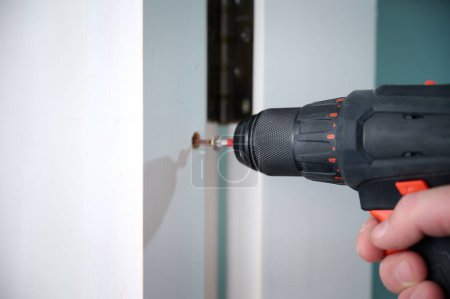 Photo for Construction worker with a screwdriver installing a door. Accessories for assembling, install furniture, repair home. Man dressed in work attire, helmet and protective glasses. Home renovation concept - Royalty Free Image
