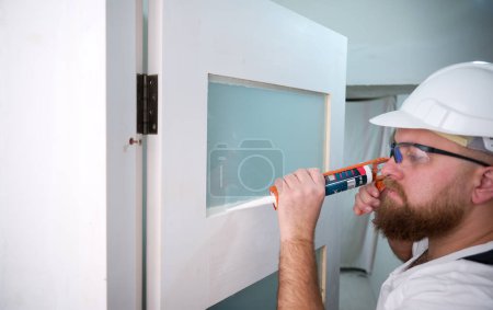 Photo for Construction worker using silicone sealant caulk. Accessories for assembling, install furniture, repair home. Man dressed in work attire, helmet and protective glasses. Caulk Sealant Application - Royalty Free Image