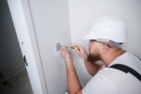 Photo for Crop view of electrician installing electric socket using screwdriver at construction site. Power socket installation. Installing a power outlet in to a plastic box on a wall. - Royalty Free Image