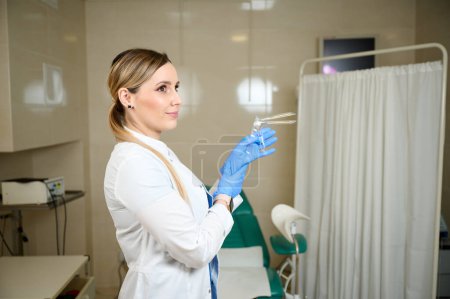 Pretty female doctor gynecologist in blue medical sterile gloves holding vaginal speculum. Women's health. Prevention illness. Early detection of cancer. Examining and consulting patient in clinic.
