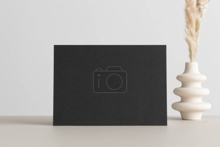 Black invitation card mockup with a  pampas decoration on the beige table. 5x7 ratio, similar to A6, A5.