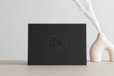 Photo for Black invitation card mockup with a pampas decoration on the beige table. 5x7 ratio, similar to A6, A5. - Royalty Free Image