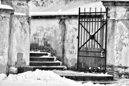 scène monochromatique d'une vieille porte et d'un mur altérés recouverts de neige, transmettant un sentiment de solitude et le passage du temps