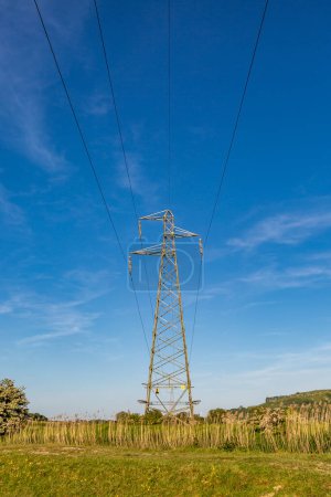 An electricity pylon in the Sussex countryside, with a blue sky overhead