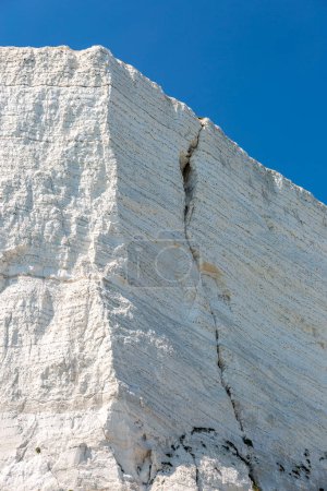 A visible crack in a chalk cliff near Beachy Head, with a blue sky overhead