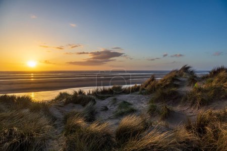 Looking out over marram grass covered sand dunes and a sandy beach, with a sunset sky overhead
