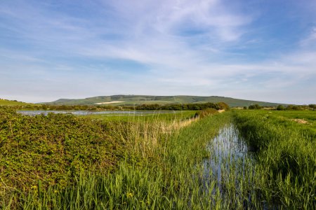 Blick entlang eines Flusses im ländlichen Sussex, mit einem überfluteten Feld in der Nähe und einem blauen Himmel über dem Kopf