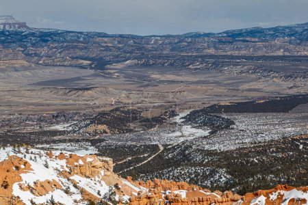 Looking out from Bryce Point over a vast landscape, on a sunny day with snow on the rocks