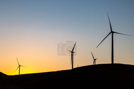 Looking up at wind turbines silhouetted against a clear sky at sunrise
