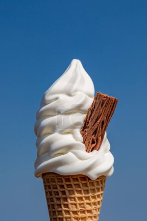 A close up of an ice cream cone with a chocolate flake against a blue sky
