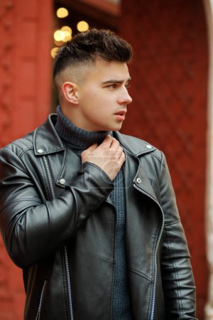 Fashionable man in a black leather jacket posing on the background of the gate.