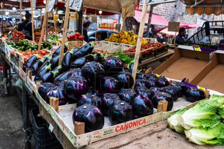 Foto de Palermo, Italia - 13 de mayo de 2023: Berenjenas en una tienda de frutas y verduras en Ballaro Market, mercado callejero de alimentos con gente alrededor en Palermo, Sicilia, Italia - Imagen libre de derechos