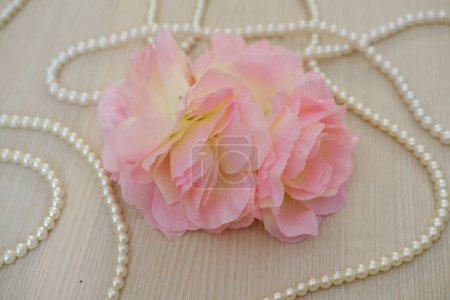 pink rose with pearl necklace on wood background, soft focus.