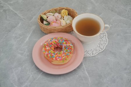 Un plato rosado con una rosquilla y una taza de té en la parte superior, creando una imagen deliciosa y apetitosa.