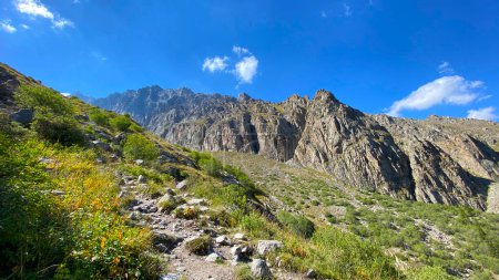 Foto de Un sendero rocoso en las montañas de Kirguistán. Parque Nacional Ala Archa. Majestuosos acantilados, crestas, picos y montañas de Kirguistán. Hermoso paisaje de montaña. Vacaciones activas de verano. - Imagen libre de derechos