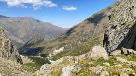 Foto de Un turista solitario está caminando a lo largo de un sendero de montaña. Una posibilidad remota. Vacaciones de verano activas. Parque Nacional Ala Archa en Kirguistán. Hermoso paisaje de montaña. Vista de rocas, crestas y picos. - Imagen libre de derechos