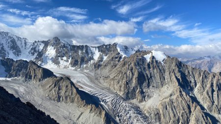 Foto de Vista de los picos nevados de las montañas kirguisas. Rocas, glaciares, cielo azul y nubes blancas. Hermoso paisaje de montaña. Parque Nacional Ala Archa en Kirguistán. Vacaciones activas de verano. - Imagen libre de derechos