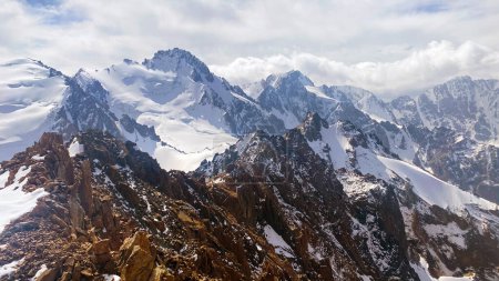 Foto de Pintoresco paisaje de montaña. Parque Nacional Ala Archa. Vista de la cresta kirguisa. Vacaciones de verano activas. Majestuosas montañas duras de Kirguistán. Picos cubiertos de nieve, rocas, colinas y laderas. - Imagen libre de derechos