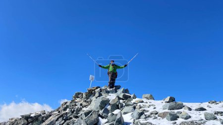 Foto de Un escalador feliz se encuentra en la cima del Monte Adygine. Parque Nacional Ala-Archa, Kirguistán. Pico rocoso cubierto de nieve. Vacaciones activas en Asia. Cielo azul. - Imagen libre de derechos