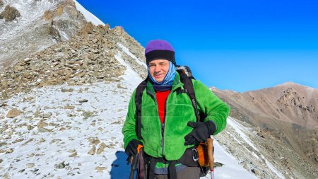 Foto de Feliz hombre sonriente escalador en las montañas. Parque Nacional Ala-Archa, Kirguistán. Vacaciones activas en Asia. Un hermoso paisaje con montañas nevadas, rocas, pendientes y picos de la cordillera de Kirguistán. - Imagen libre de derechos