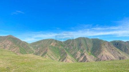Beautiful views around the Konorchek canyons in Kyrgyzstan. The mountains are covered with green grass and rocks. The sky is clear and blue. The landscape is peaceful and serene, the mountains rise above the grassy plain