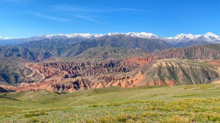 Aerial view of the Konorchek canyons in Kyrgyzstan. An amazing mountain range with a snowy peak and a green field in the foreground. Beautiful mountain summer landscape