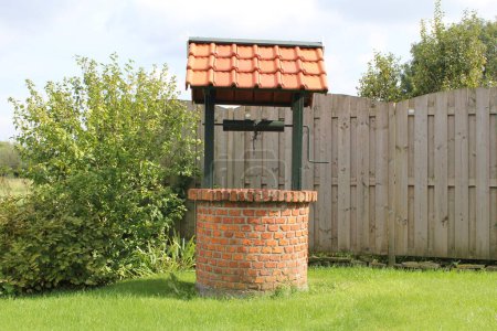 Téléchargez les photos : Un puits d'eau historique à herbe verte dans un jardin pour arroser les fleurs et les légumes - en image libre de droit