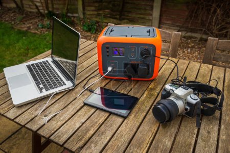 Photo for Portable power station solar electricity generator with laptop, tablet and camera electronic devices charging. Wireless charging lithium battery backup for power outage emergencies outdoors or camping - Royalty Free Image