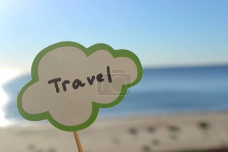 Photo for Stick with paper speech bubble with words Travel on background blue sea, sky, sandy beach on sunny summer day. Text-balloons with text from letters. Concept, symbol, sign vacation travel tourism rest - Royalty Free Image