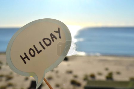 Photo for Stick with paper speech bubble with words Holiday on background blue sea, sky, sandy beach on sunny summer day. Text-balloons with text from letters. Concept, symbol, sign vacation travel tourism rest - Royalty Free Image