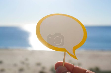 Photo for Stick with paper empty speech bubble on background blue sea, sky, sandy beach in hand on sunny summer day. Text-balloons with space for text. Concept, symbol, sign vacation travel tourism rest holiday - Royalty Free Image