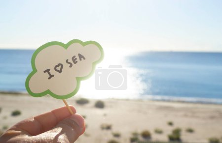 Photo for Stick with paper speech bubble with words I love sea on background blue sea sky sandy beach on sunny summer day. Text-balloons with text from letters. Concept symbol sign vacation travel tourism rest - Royalty Free Image