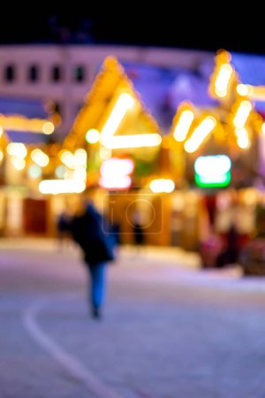 Photo for Blurred background. People walk in city square on winter night. Black silhouettes of people walking near houses decorated luminous illumination. White light bokeh blur spots from glowing house lights - Royalty Free Image