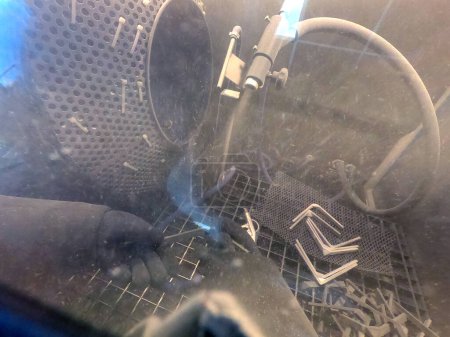 Téléchargez les photos : Shot blasting. Shot blasting of model printed on 3D printer from polyamide powder. A worker in sealed rubber gloves cleans the object by shot blasting in a shot blasting chamber. Industrial machine - en image libre de droit